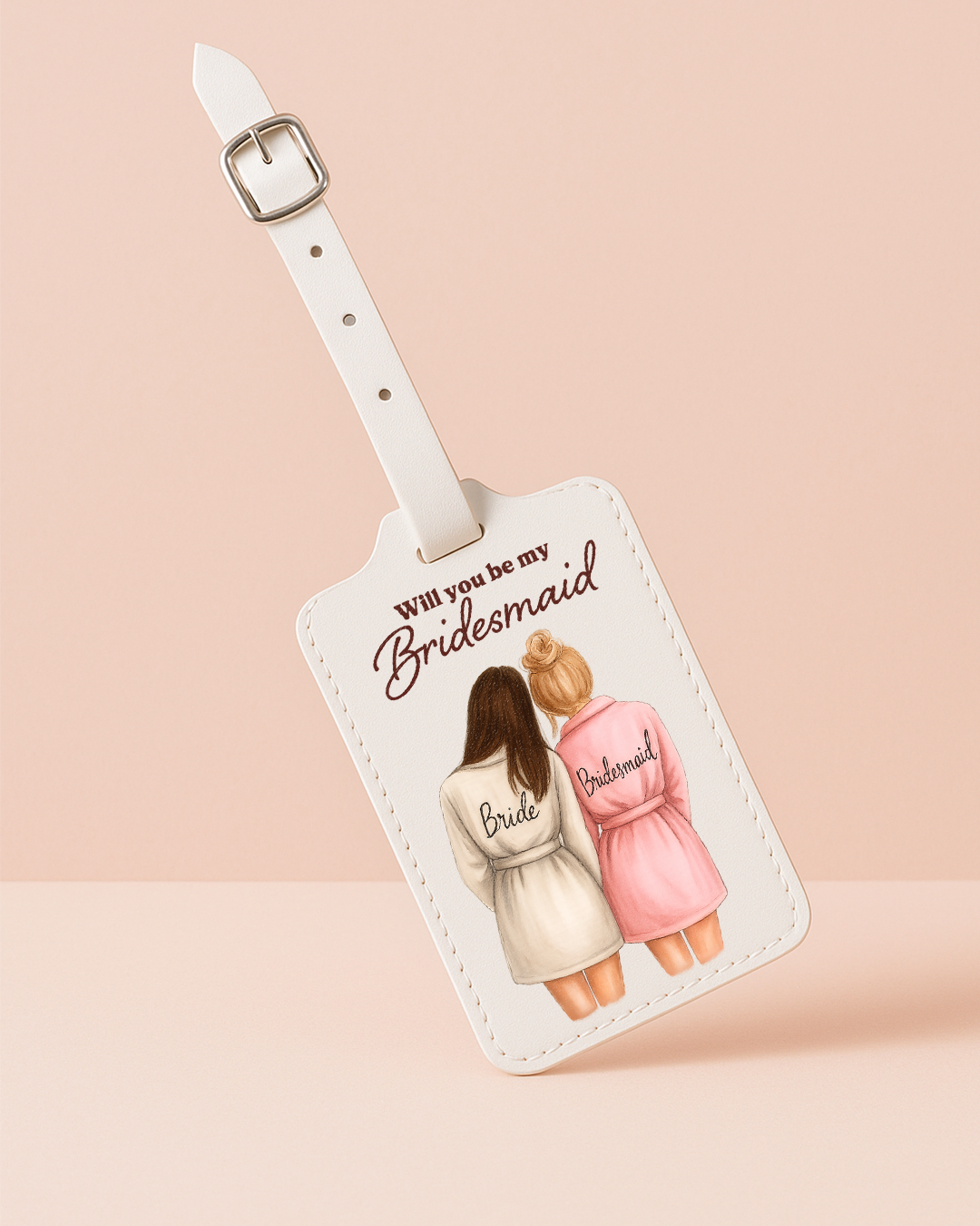 Luggage tag with illustration of two women in robes and text 'Will you be my Bridesmaid' on a beige background